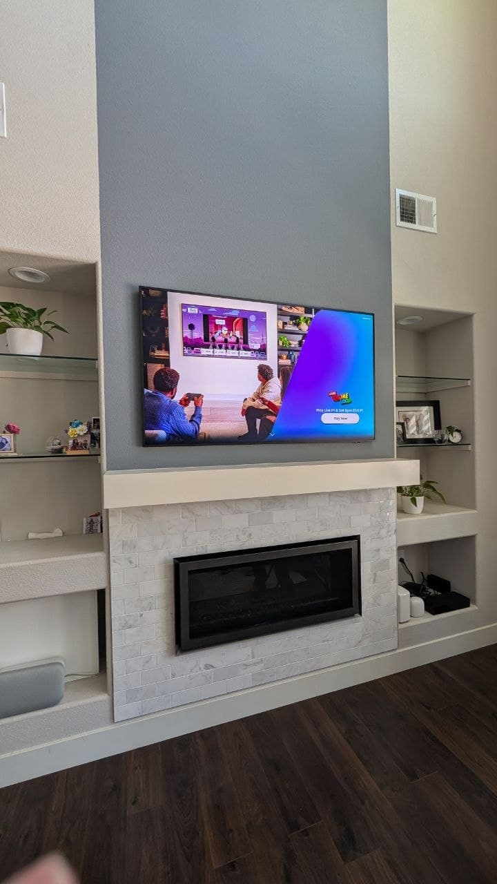 65-inch Samsung Frame TV mounted above modern linear fireplace with marble tile and built-in shelving in West Roseville, CA