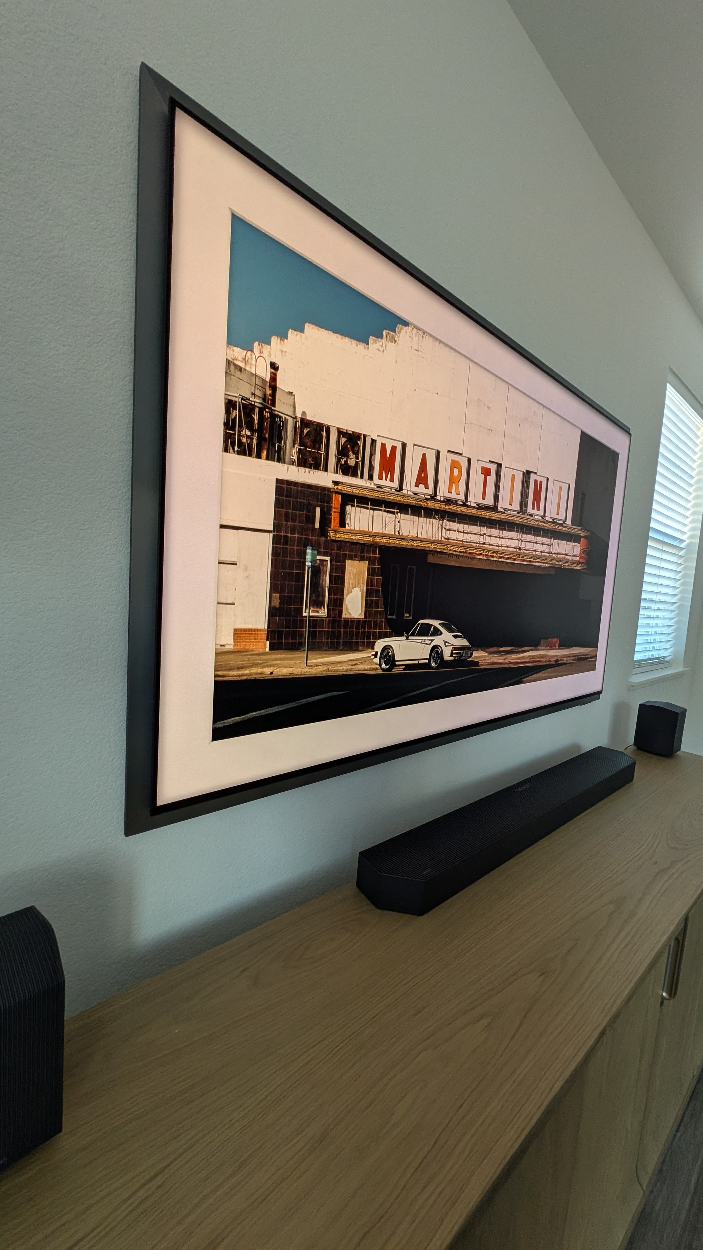 Side angle of Samsung S95F displaying ambient art mode with Q990F soundbar on oak credenza in Granite Bay, CA